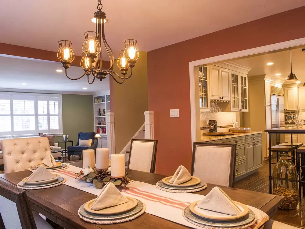 A large wood table in an open-space kitchen with orange walls